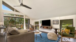 Ein geräumiger Wohnbereich mit großem Fenster, Deckenventilator und einem flachbildfernseher an der Wand.