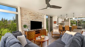 Ein modernes Wohnzimmer mit großem Fernseher, grauen Sofas, einem Holztisch und einer Steinwand.