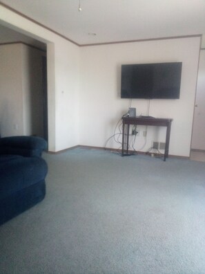 A room with a flat-screen TV mounted on the wall, a small wooden table with electronic devices, and a dark-colored sofa.