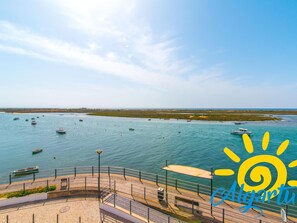 A waterfront promenade with a paved walkway, benches, and a railing overlooking a body of water with several boats. - Apartamento T0 Vista Mar Vista Ria Formosa (Tavira)