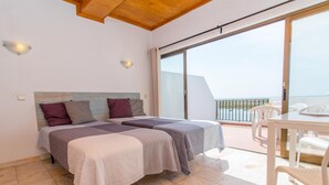 A bedroom with two beds, a balcony with a table and chairs, and a view of the sea. - Apartamento T0 Vista Mar Vista Ria Formosa (Tavira)