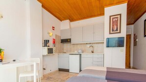 A compact room with a bed, a desk, a chair, a kitchenette, and a television. - Apartamento T0 Vista Mar Vista Ria Formosa (Tavira)