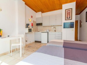 Ein kleines Zimmer mit Bett, Schreibtisch, Stuhl, Küchenzeile und Fernseher.
