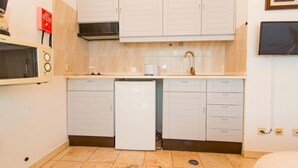 A compact kitchen with white cabinets, a microwave, a small refrigerator, and a sink. - Apartamento T0 Vista Mar Vista Ria Formosa (Tavira)