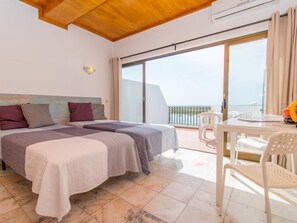 A hotel room with two beds, a balcony with a table and chairs, and a view of the sea. - Apartamento T0 Vista Mar Vista Ria Formosa (Tavira)