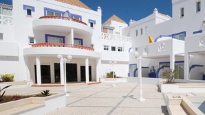 Un patio con suelo de baldosas, edificios blancos con detalles azules y un espacio central abierto.