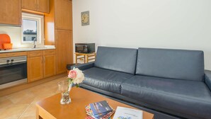 Un espacio habitable compacto con kitchenette, un sofá, una mesa de centro y un reloj en la pared.