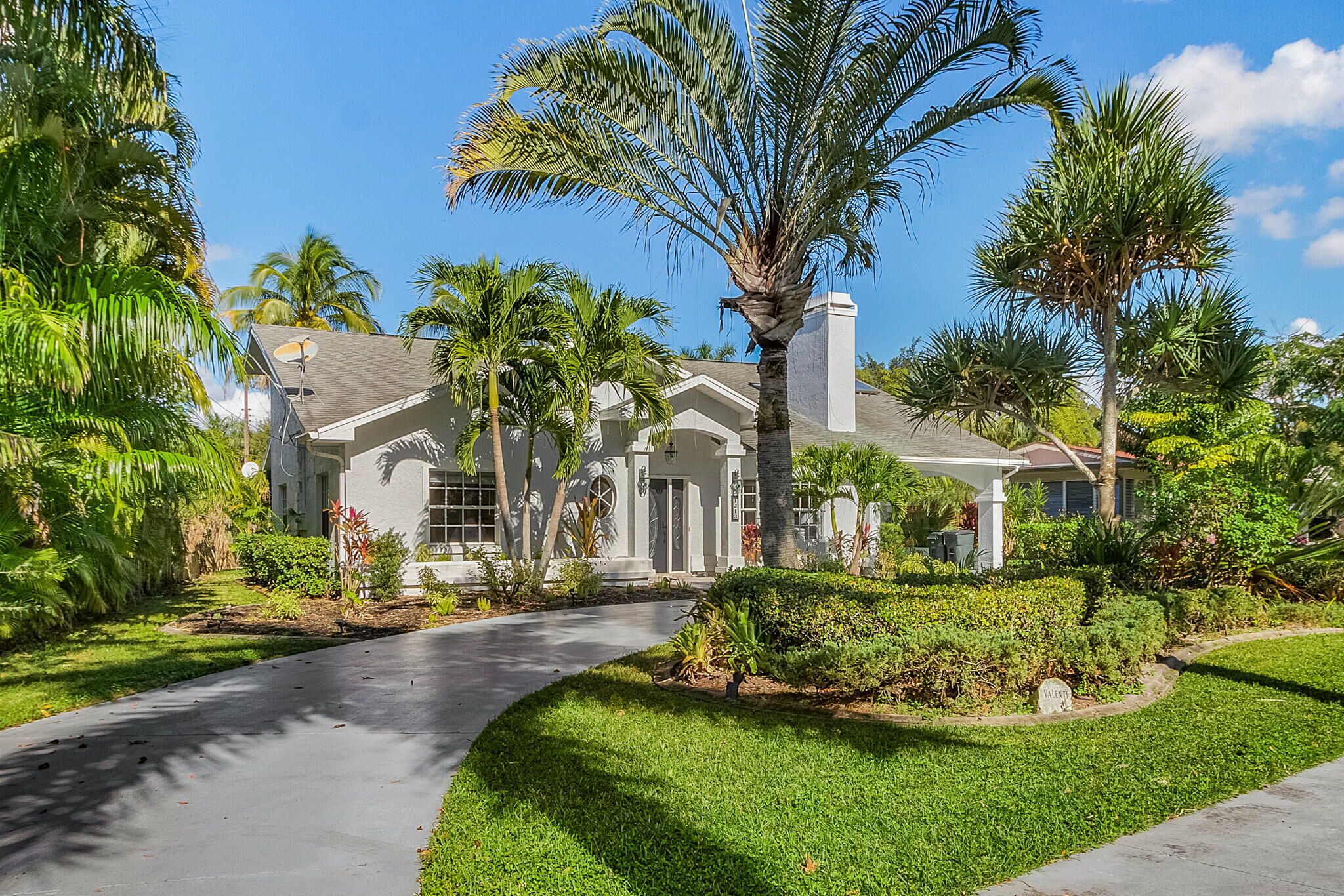 A residential house with a driveway, palm trees, and a well-maintained lawn.