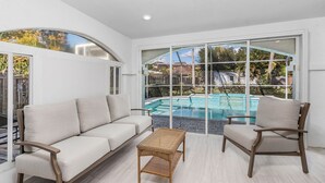 A modern living room with a sofa, armchairs, and a coffee table, overlooking a swimming pool. - Newly Updated!  RiverView Retreat  Historic Fort Myers, FL 10 guests, Spa & pool (Fort Myers)