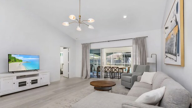 A modern living room with a flat-screen TV, a sofa, a coffee table, and a chandelier. - Newly Updated!  RiverView Retreat  Historic Fort Myers, FL 10 guests, Spa & pool (Fort Myers)