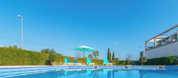 Ein Swimmingpool mit Liegestühlen und einem Sonnenschirm, umgeben von Grünflächen und einem modernen Gebäude.
