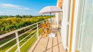 En balkon med et bord, stole og en hvid parasol, samt udsigt over det grønne omkringliggende landskab.