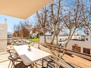 Ein Balkon mit Tisch und Stühlen, der auf einen Wohnbereich mit weißen Gebäuden und Bäumen blickt.
