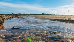 A riverbank with clear water and rocks, a sandy beach, and a clear sky. - Pegada Apartamento T3 Luxo (Tavira)