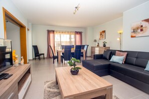 A modern living room with a sofa, coffee table, TV, and dining area. - Pegada Apartamento T3 Luxo (Tavira)
