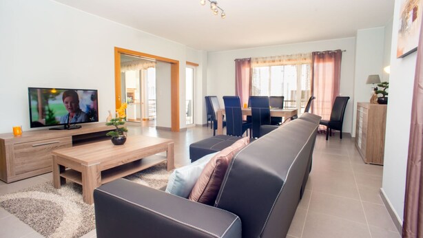 A modern living room with a TV, sofa, coffee table, and dining area. - Pegada Apartamento T3 Luxo (Tavira)