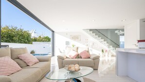Ein modernes Wohnzimmer mit einem Glastisch, beigefarbenen Sofas und einer Treppe, die zu einer oberen Ebene führt.