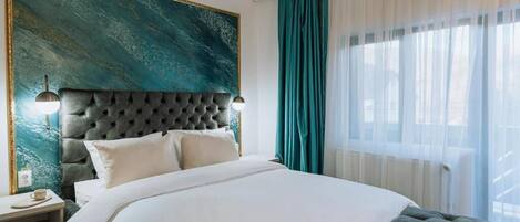 A modern hotel room with a large bed, a tufted headboard, a large abstract painting, and a view of the outdoors through sheer curtains.