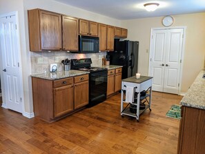 Kitchen with a black microwave, refrigerator, and oven, plus a small table and a door.