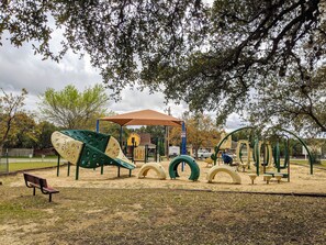 Explore a playground with slides, swings, and climbing elements, set amidst a natural backdrop of trees and a shaded seating area.
