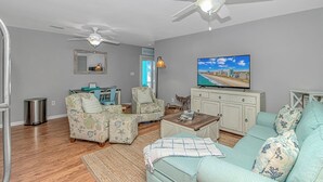 Uma sala de estar com sofá, poltronas, mesa de centro, televisão e ventiladores de teto.
