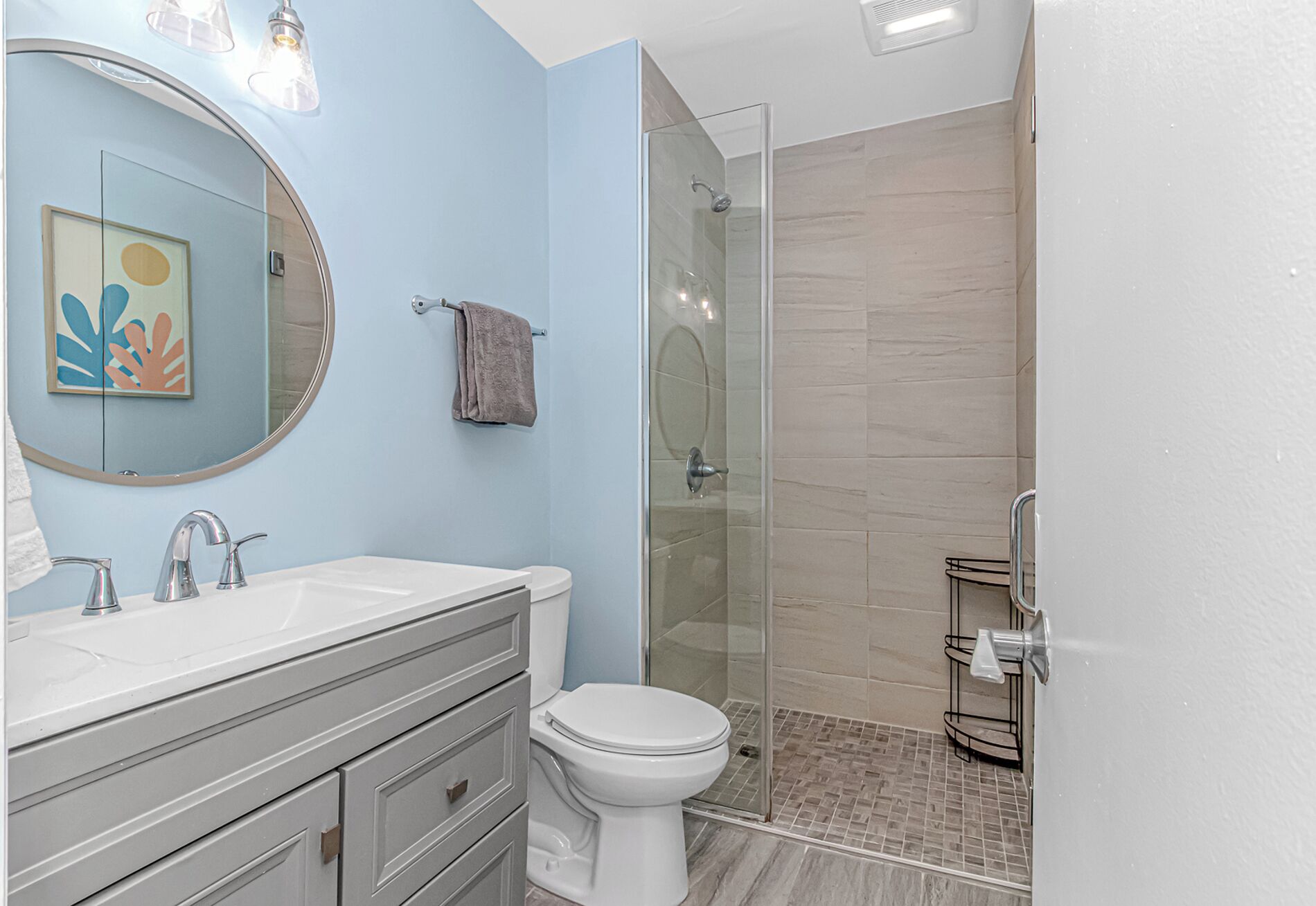 Un baño moderno con ducha envuelta en vidrio, inodoro blanco y tocador con espejo y lavamanos.