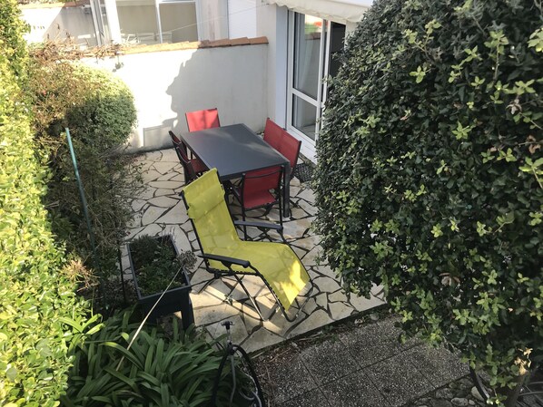 Een buitenpatio met een tafel en stoelen, omringd door groen en een stenen vloer.