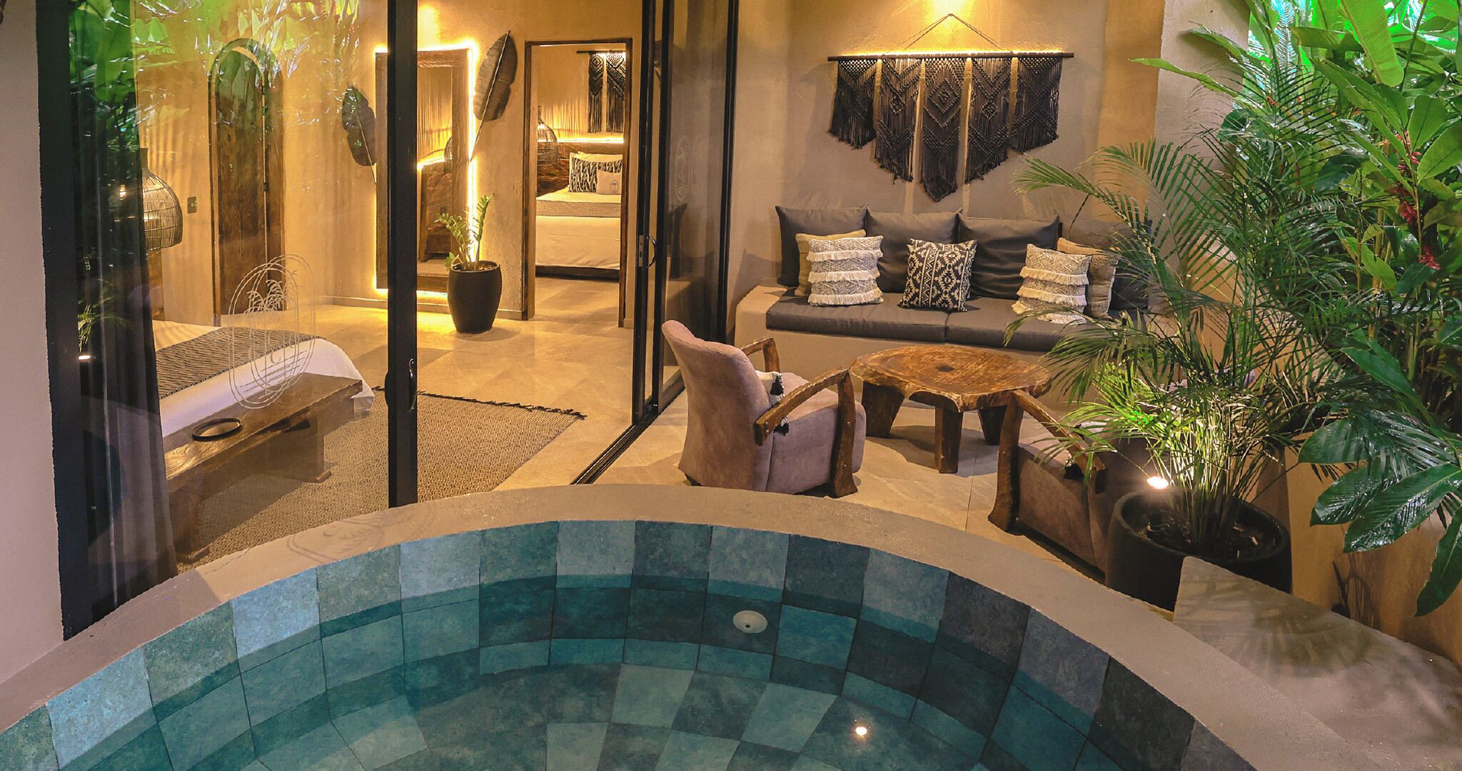 A cozy indoor pool area with a seating area, a sofa with patterned cushions, and various plants.