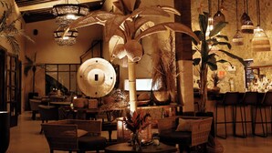 A spacious lobby with a large palm tree centerpiece, wicker furniture, and hanging pendant lights.
