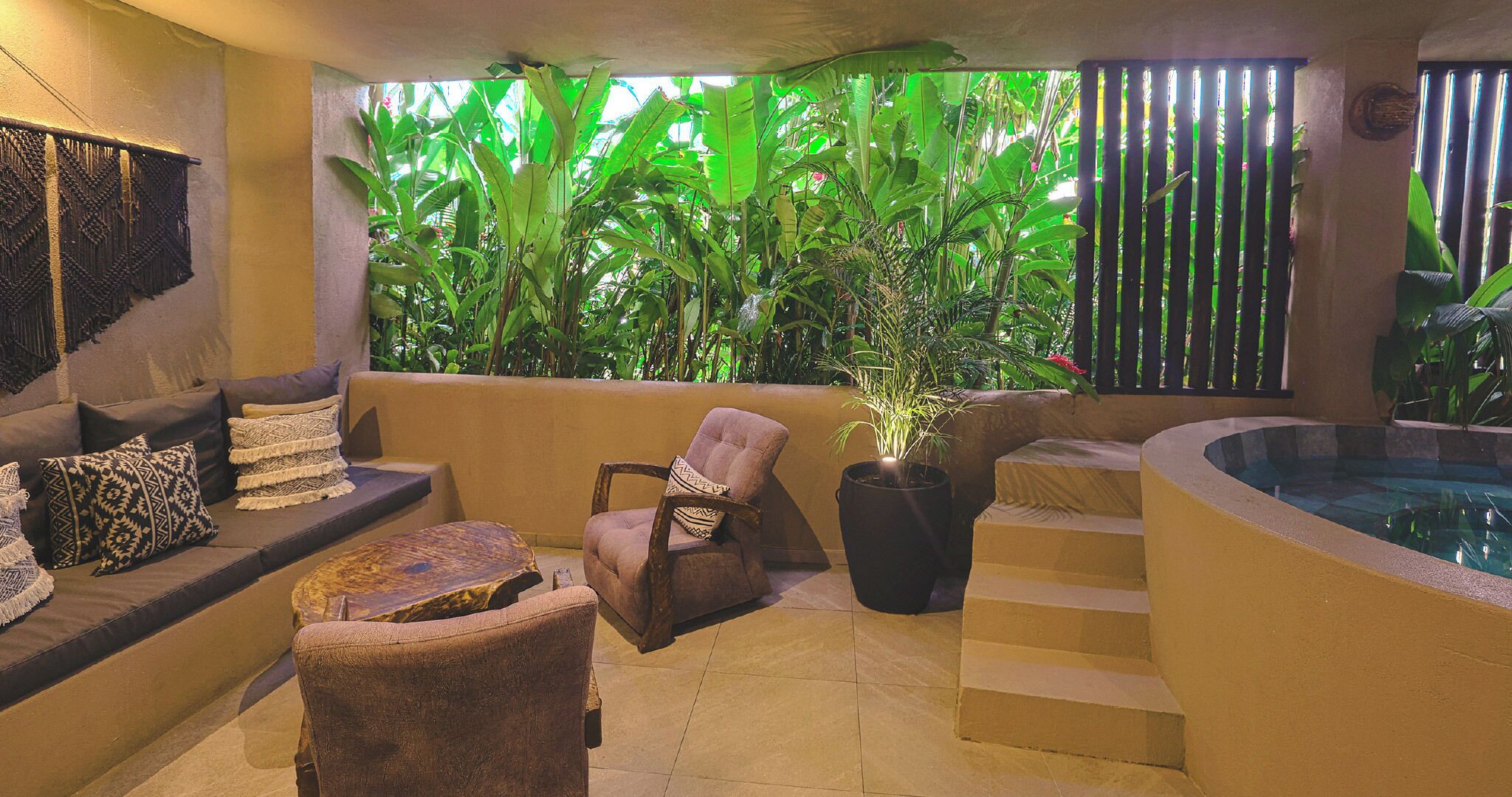 Un área de spa con zona de estar, una silla, una planta grande en maceta y un jacuzzi.