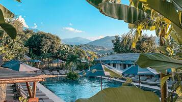 A pool area with lounge chairs and umbrellas, surrounded by tropical foliage and a mountainous backdrop.
