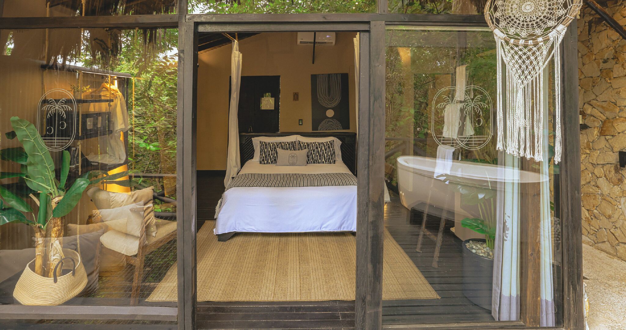 A bedroom with a bed, a bathroom with a bathtub, and a glass door leading to a balcony with plants.