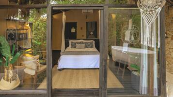 A bedroom with a bed, a bathroom with a bathtub, and a glass door leading to a balcony with plants.