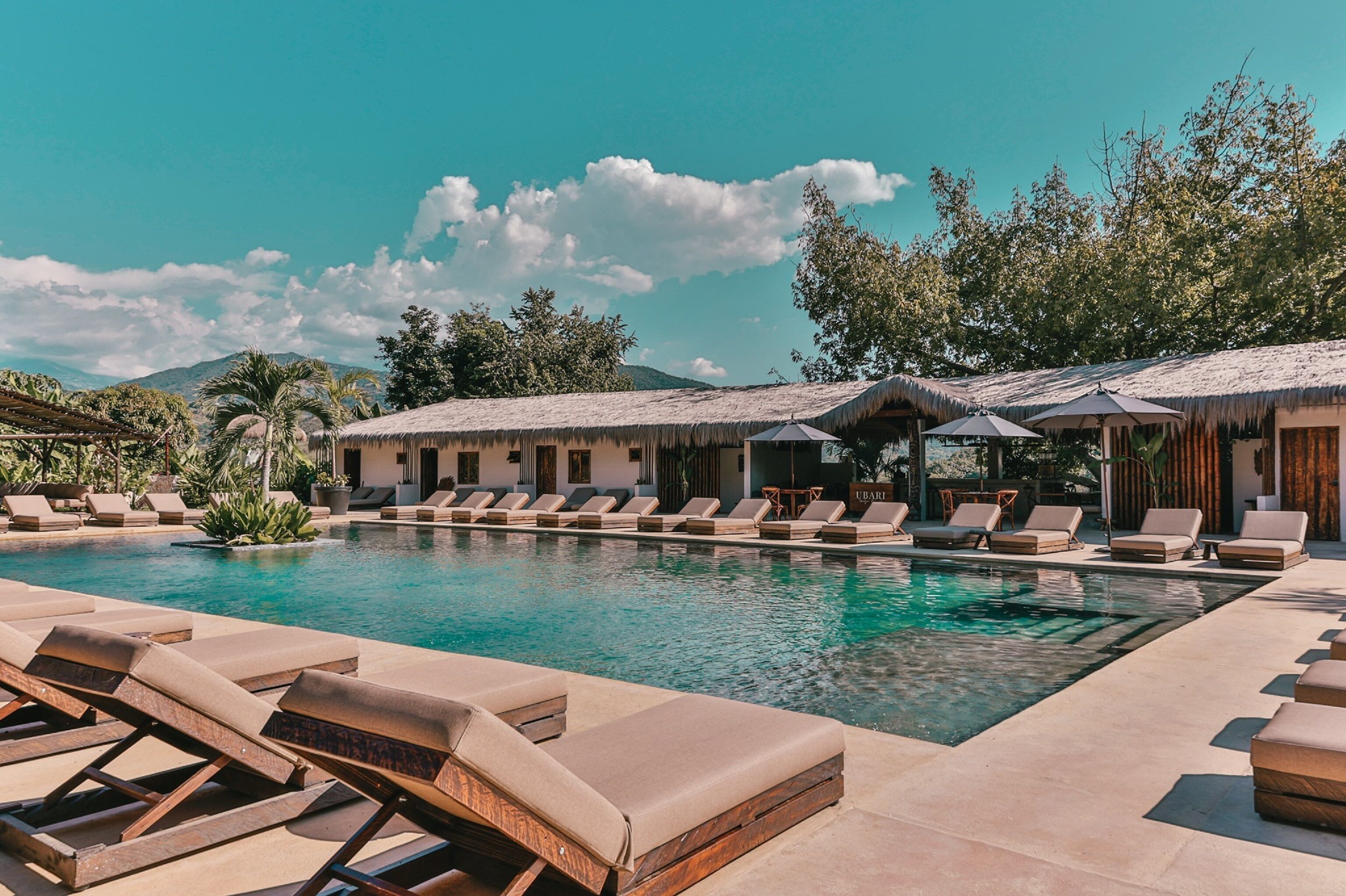A pool area with lounge chairs and thatched-roof structures.