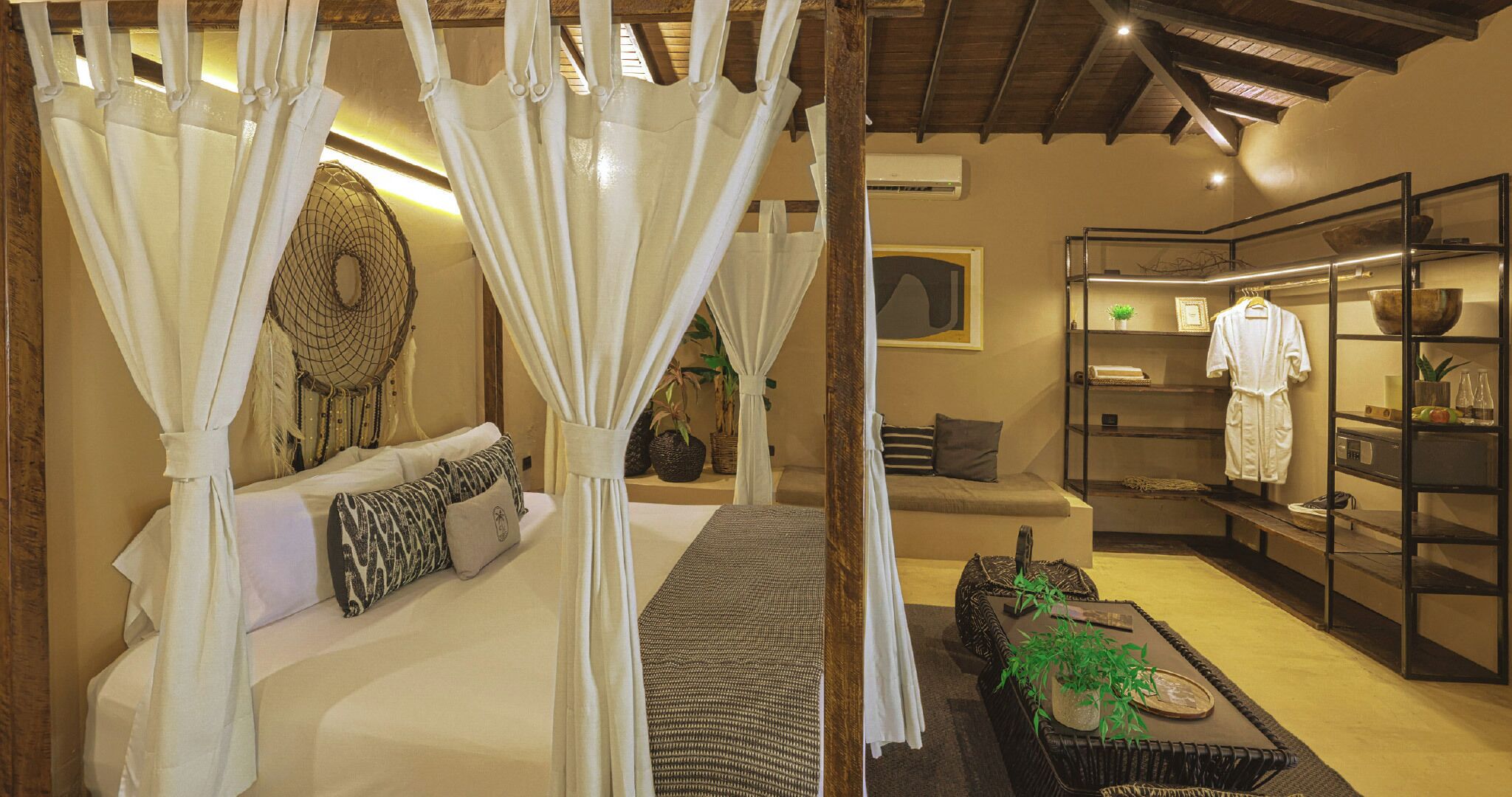 A bedroom with a canopy bed, a sofa, a coffee table, and a shelf with robes and toiletries.