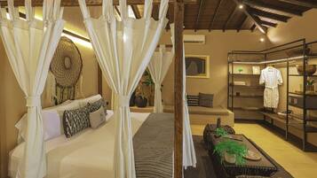 A bedroom with a canopy bed, a sofa, a coffee table, and a shelf with robes and toiletries.