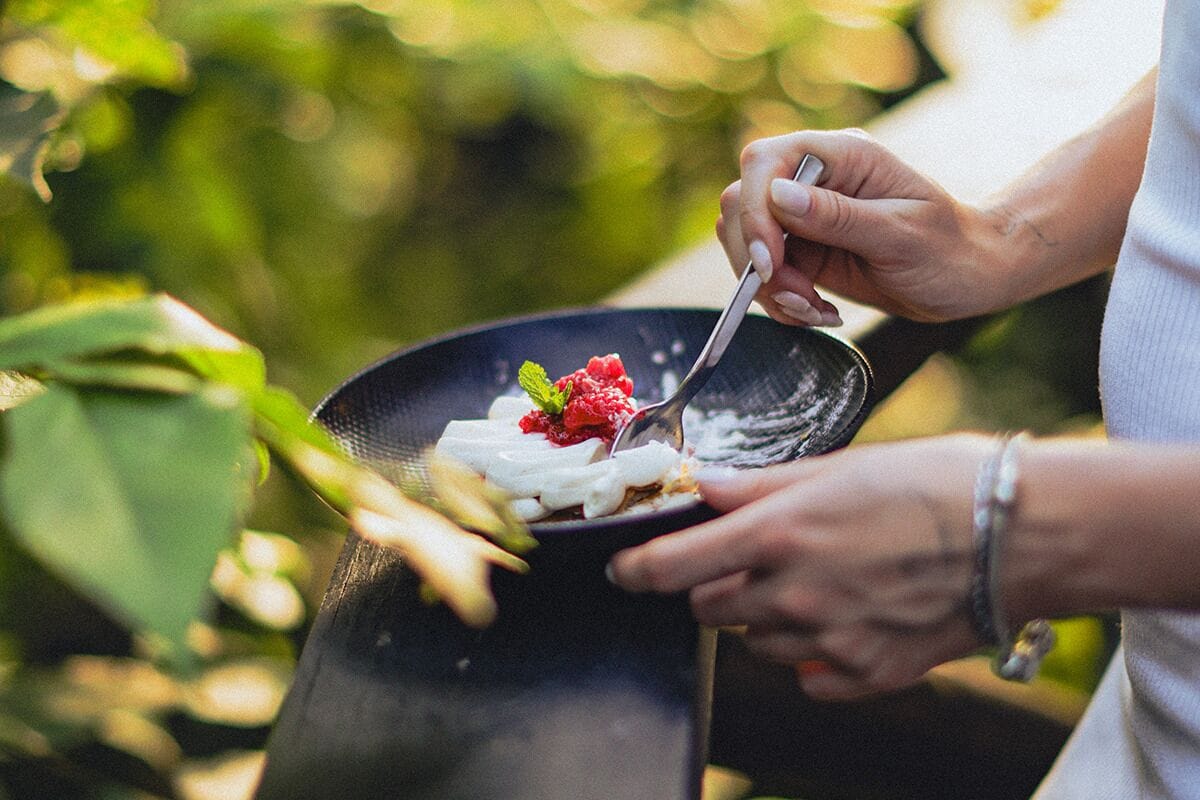 A person holding a bowl with a dessert, possibly a fruit tart, with a spoon.