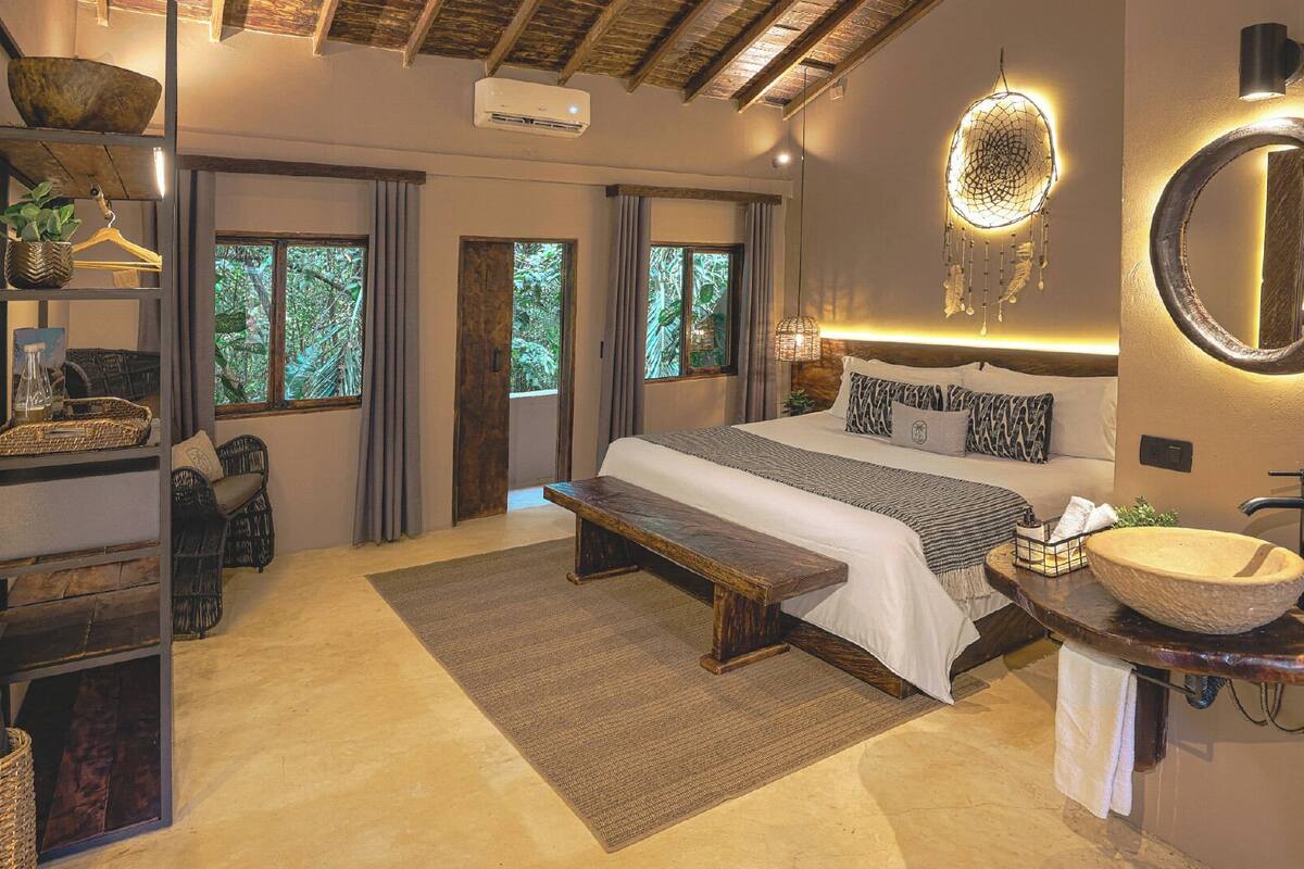 Une chambre à coucher avec un grand lit, une table de chevet dotée d’un lavabo en forme de coupe, un banc et une étagère avec des paniers.