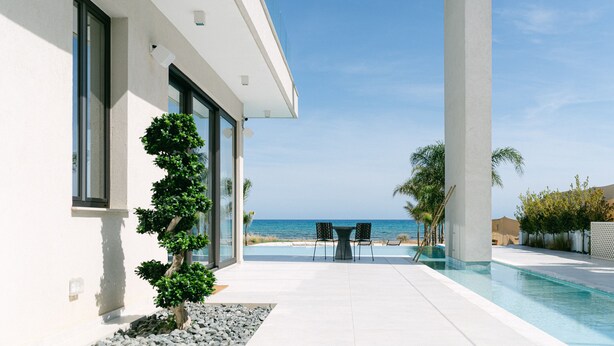 Een modern huis met een zwembad, uitzicht op zee en een terras met stoelen.