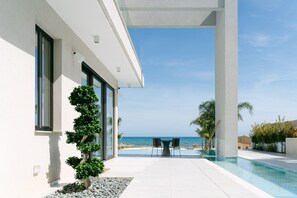 A modern house with a pool, a view of the ocean, and a patio with chairs. - Eros Cyprus: Sea Front Luxury Villa with option to add catering and services (Sotira)