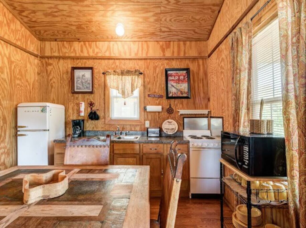 A compact kitchen with wooden walls, a refrigerator, a stove, and a microwave.