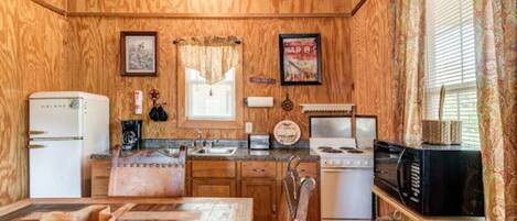 A compact kitchen with wooden walls, a refrigerator, a stove, and a microwave.