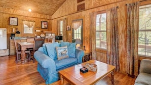 Interior acogedor de una cabaña con techo de madera, una zona de comedor, un sofá azul y una mesa de centro de madera.