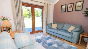 Een woonkamer met een blauwe bank, een ruitdessinbank, een houten salontafel en een blauw gestreept tapijt. Er is een deur naar een tuin.