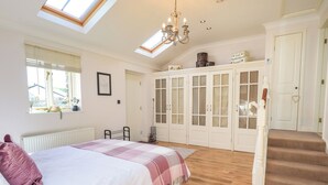 Een slaapkamer met een groot bed, dakraam, een kroonluchter, een kledingkast en een trap.