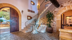 A stone-floored lobby with a wooden door, a staircase with a railing, and a large potted plant. - Esturonet, Finca 5EstrellasHome Mallorca (Manacor)
