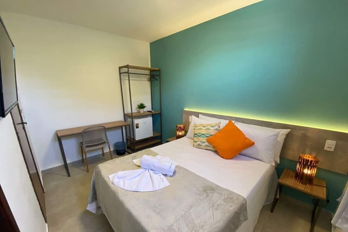 Hotellihuone, jossa on sänky, työpöytä, tuoli, pieni pöytä ja yöpöytä.