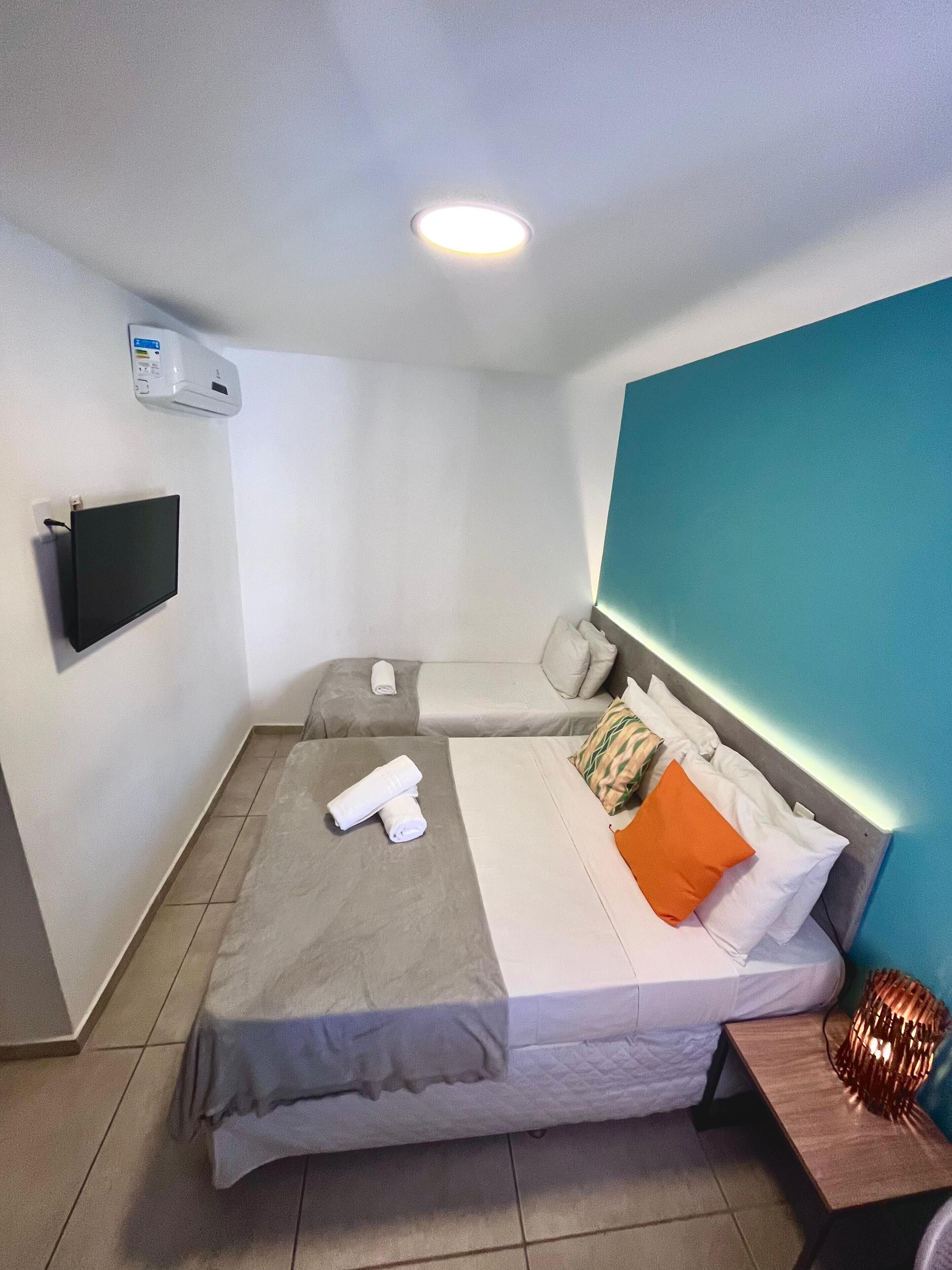 A hotel room with a bed, a TV, a heater, and a nightstand with a lamp.