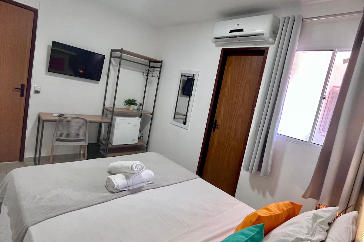 Hotellihuone, jossa on kaksi sänkyä, työpöytä tietokoneella, televisio ja ilmastointilaite.