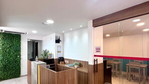 A modern reception area with a wooden reception desk, a green wall, and a glass partition with a red stripe. - Pousada Mirante dos Corais (Ipojuca)